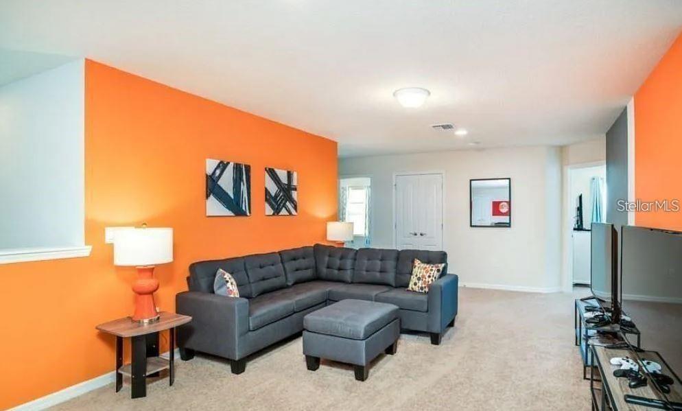 A living room features a gray sectional sofa, an orange accent wall, and beige carpeting — 8817 CORCOVADO DRIVE, KISSIMMEE, FL