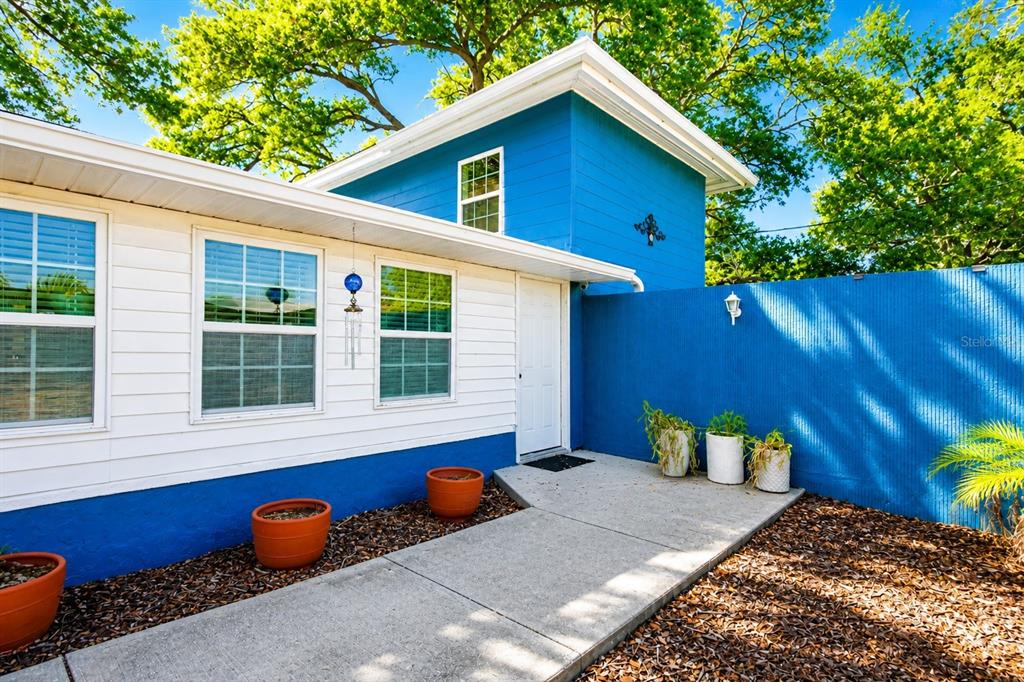 A blue and white house exterior features a concrete walkway, potted plants, and a door — 4720 WELCH CAUSEWAY, ST PETERSBURG, FL