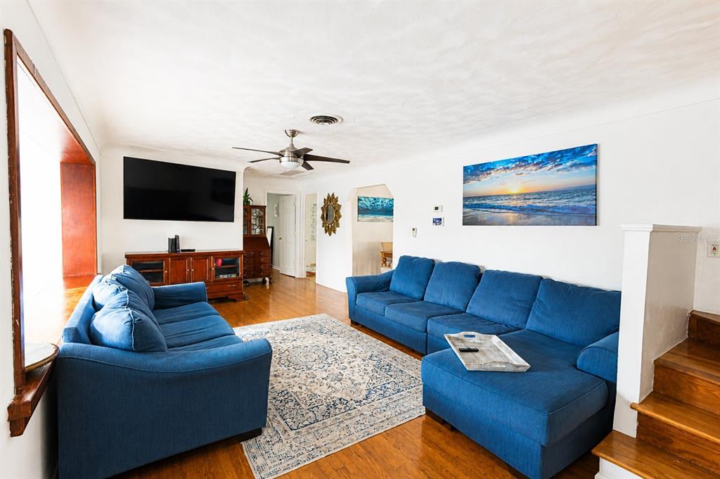A living room features two blue sofas, a patterned area rug, and hardwood flooring — 4720 WELCH CAUSEWAY, ST PETERSBURG, FL