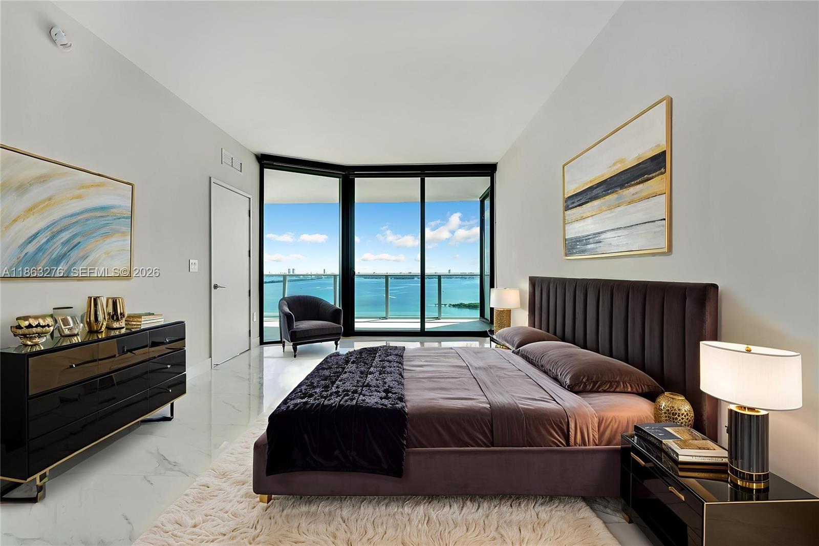 A modern bedroom features a dark upholstered bed, marble floors, and floor-to-ceiling windows overlooking water — 725 NE 24th, Miami FL 33137, MIAMI, FL