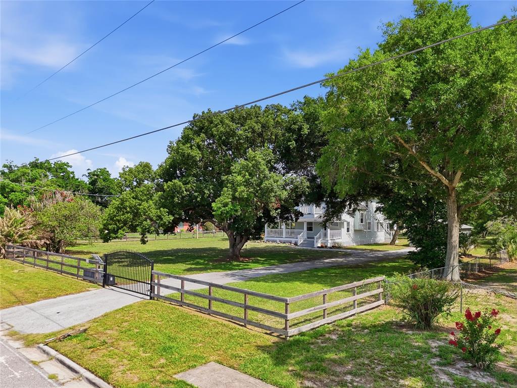 A white house with a porch sits behind a gated fence and large trees — 545 E HAINES BOULEVARD, LAKE ALFRED, FL