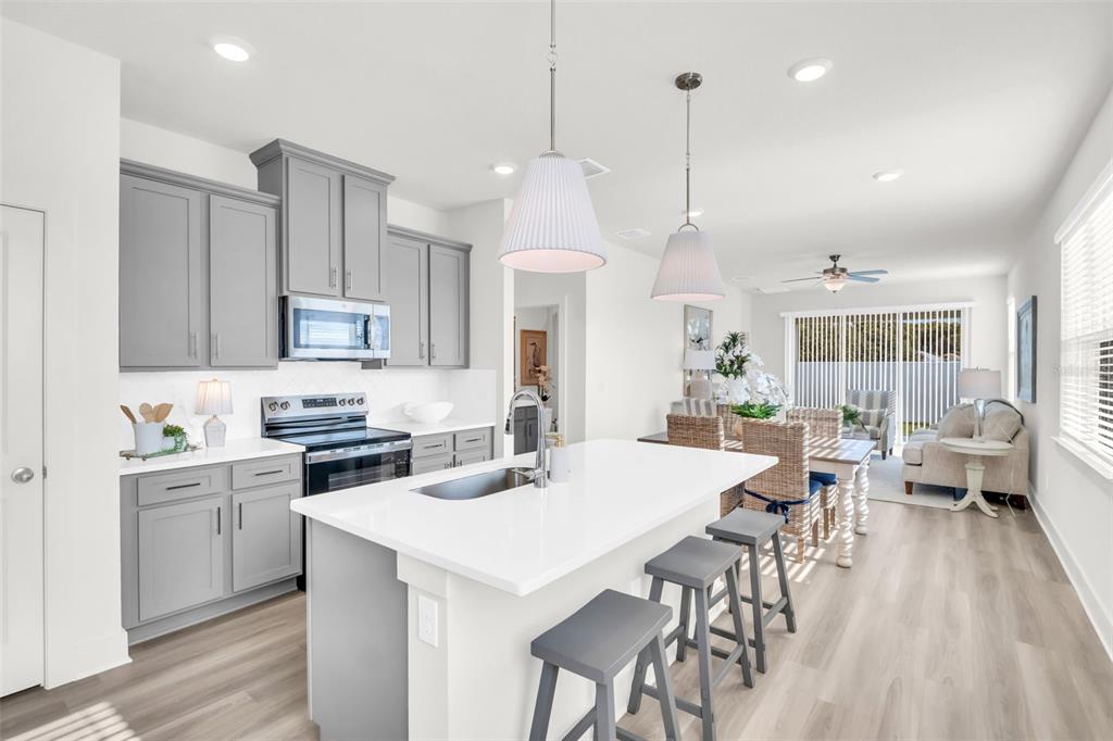 A modern kitchen features gray cabinets, a white quartz island, and an open-concept dining area — 7994 CHANDLER LAKE COURT Lot 16, HUDSON, FL