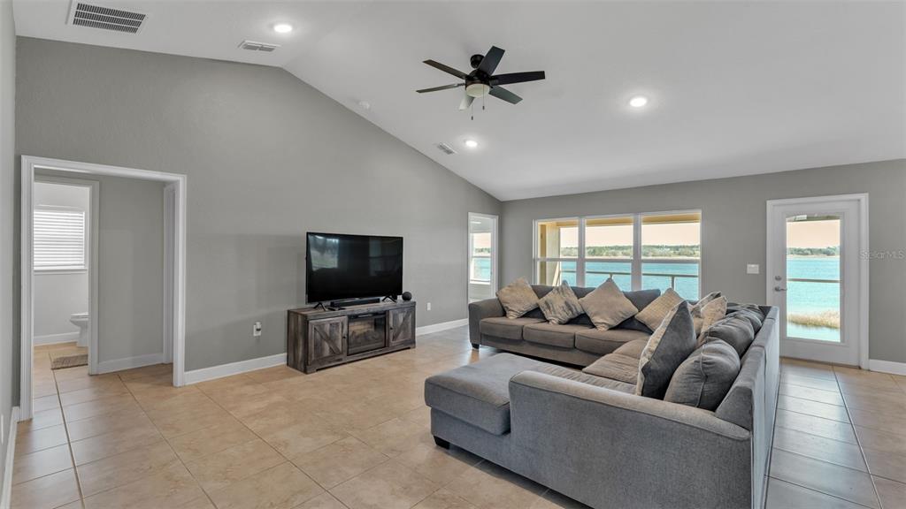 A living room with vaulted ceilings, tile flooring, a gray sectional sofa, and lake views — 4724 BROOKSHIRE COURT, LAKE WALES, FL