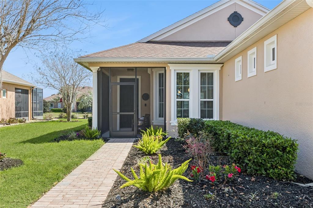 A paved walkway leads to the screened front entryway of a tan house with landscaping — 371 SALT MARSH LANE, GROVELAND, FL