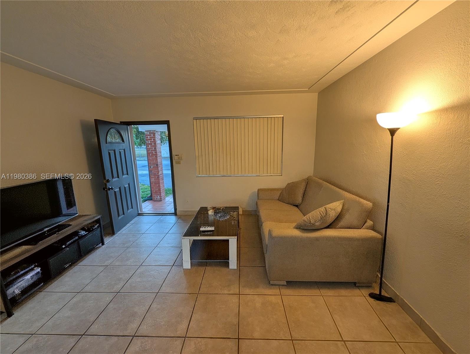 A living room features tile flooring, a beige sofa, a coffee table, and an open door — 1037 SW 76th Ave # 1037, Miami FL 33144, MIAMI, FL