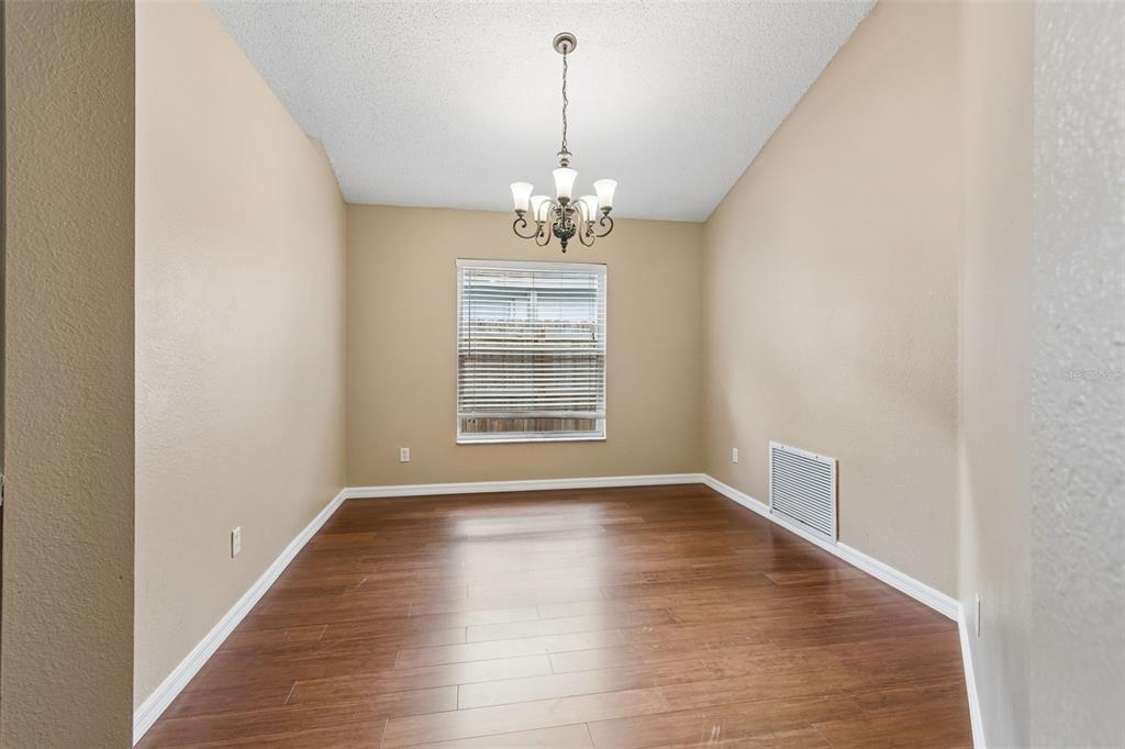 An empty dining room features hardwood floors, beige walls, a chandelier, and a single window — 5646 PADDOCK TRAIL DRIVE, TAMPA, FL