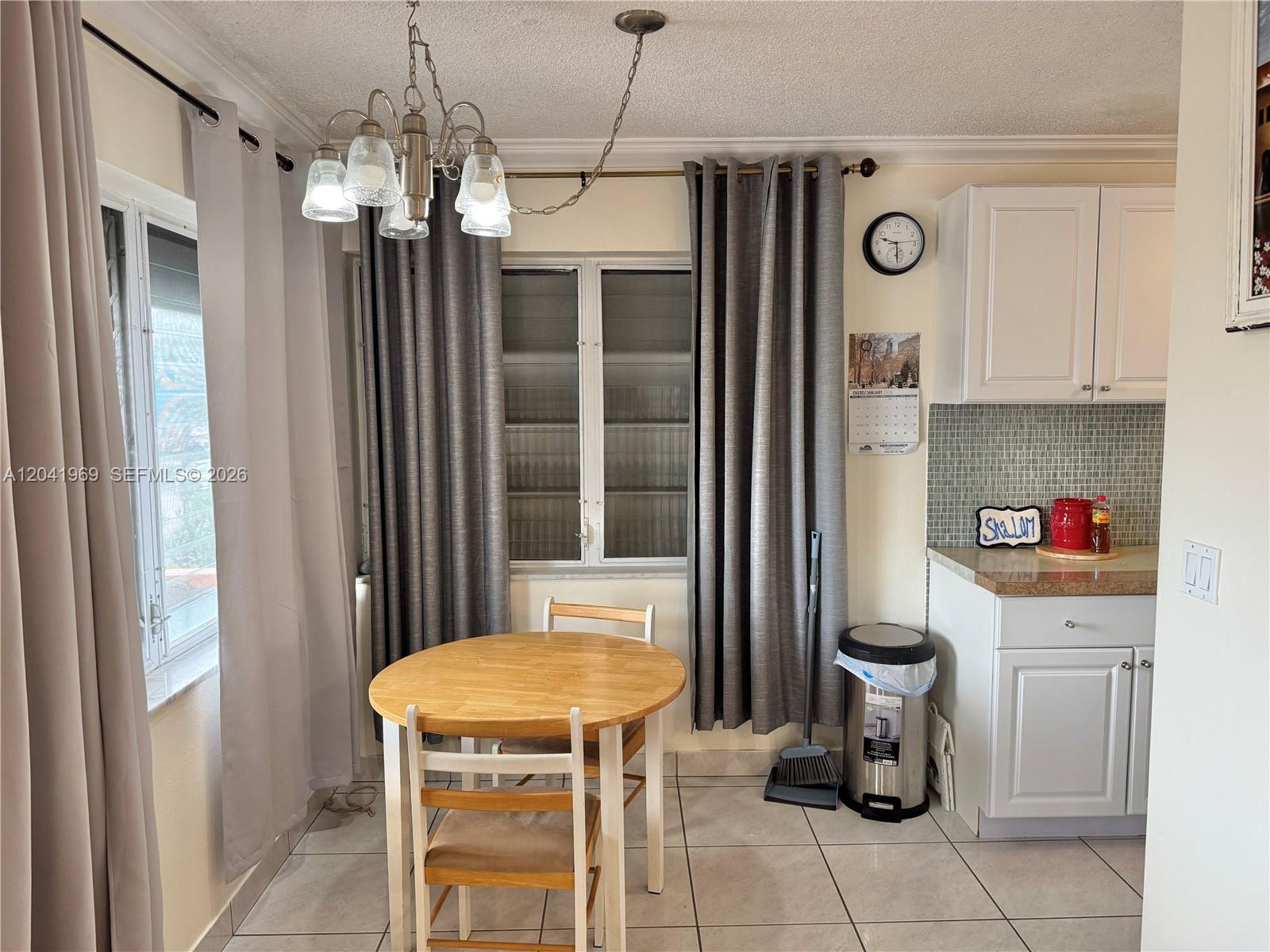 A dining area features a round wooden table, chairs, gray curtains, and white kitchen cabinets — 920 SW 11th Ave # 11, Hallandale Beach FL 33009, HALLANDALE BEACH, FL