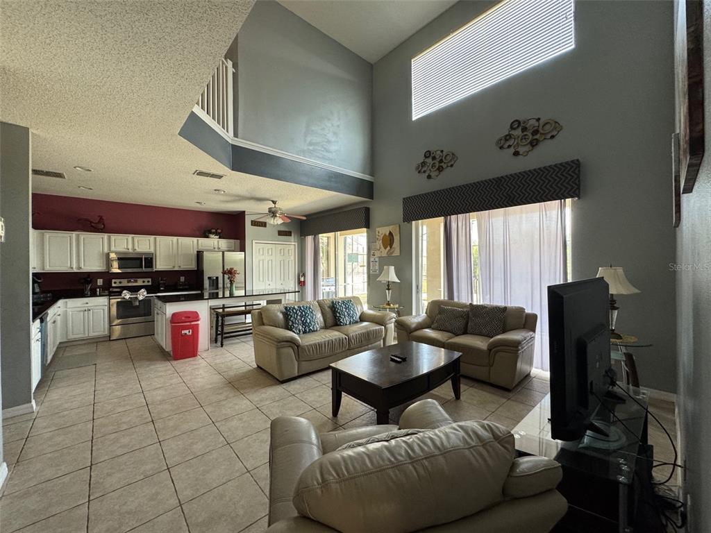 An open-concept living room and kitchen with high ceilings, tile floors, and neutral furniture — 2677 EMERALD ISLAND BOULEVARD, KISSIMMEE, FL