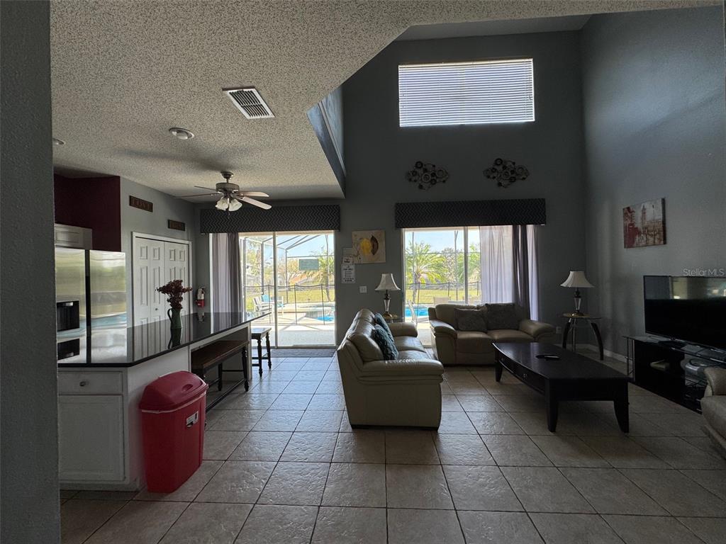 A living room with tile floors, a high ceiling, and a kitchen island overlooks a pool — 2677 EMERALD ISLAND BOULEVARD, KISSIMMEE, FL