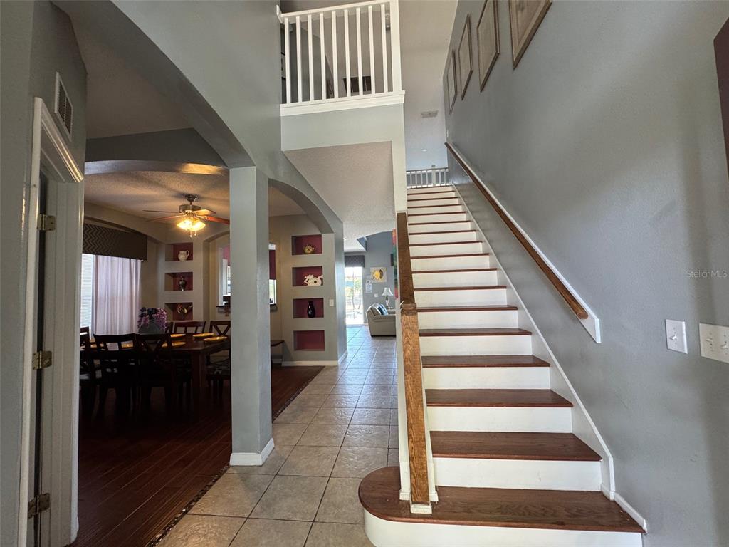 An entryway features a staircase with wooden treads, tiled floors, and an adjacent dining area — 2677 EMERALD ISLAND BOULEVARD, KISSIMMEE, FL