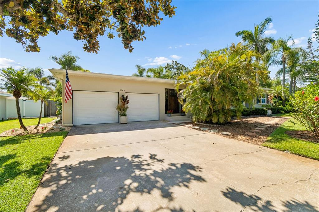 A single-story house with a two-car garage, a concrete driveway, and lush tropical landscaping — 1743 EAGLES NEST DRIVE, BELLEAIR, FL