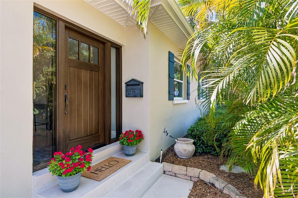 A wooden front door with sidelights sits on a porch with potted flowers and a mat — 1743 EAGLES NEST DRIVE, BELLEAIR, FL