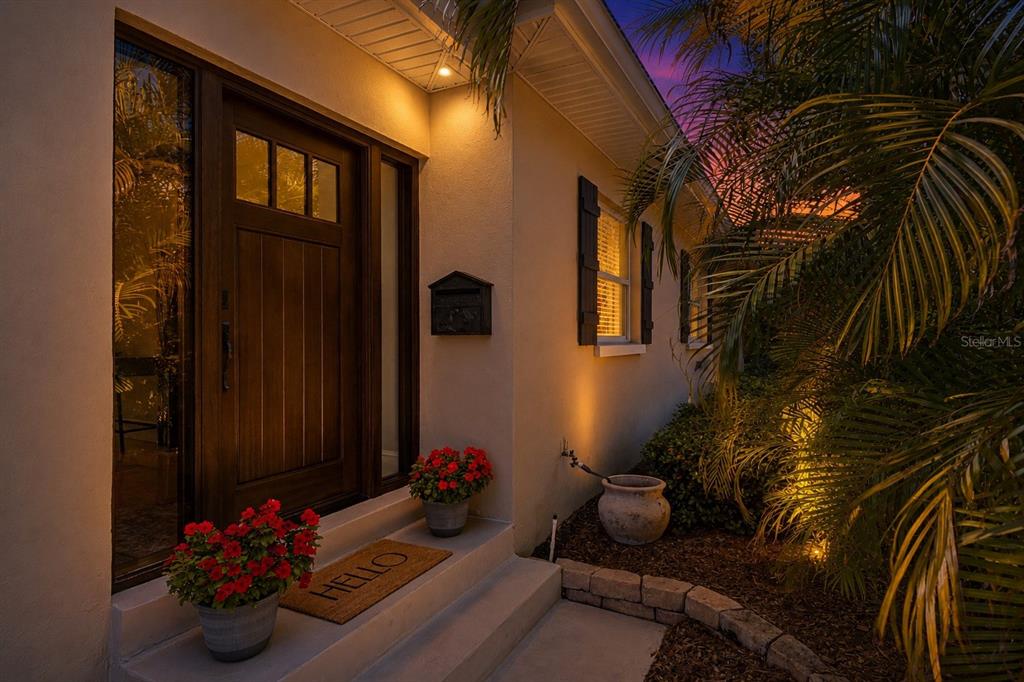 A front entrance with a dark wood door, a welcome mat, and potted red flowers — 1743 EAGLES NEST DRIVE, BELLEAIR, FL
