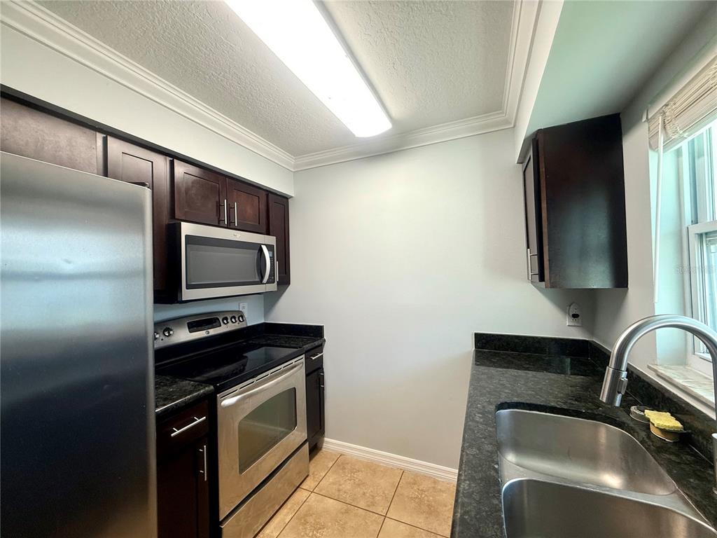 A galley kitchen features dark wood cabinets, stainless steel appliances, and black granite countertops — 209 DORCHESTER SQUARE UNIT 209, LAKE MARY, FL