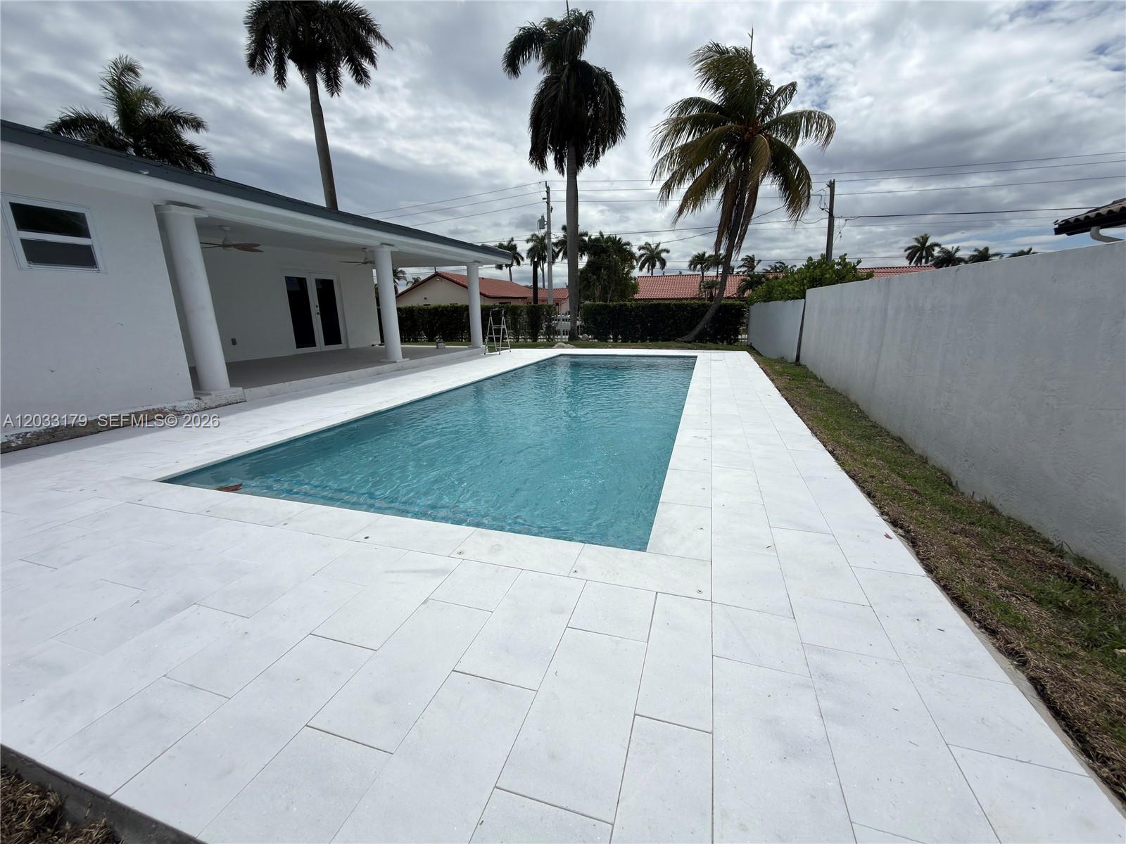 A rectangular swimming pool is surrounded by white stone pavers next to a white house — 13895 SW 22nd St, Miami FL 33175, MIAMI, FL