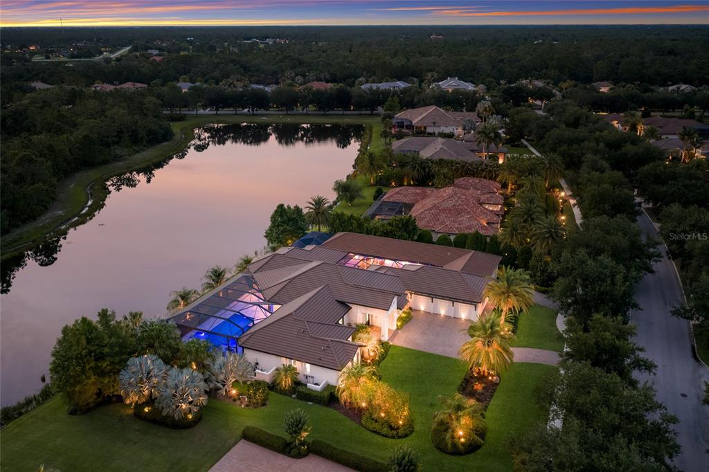 An aerial view shows a large house with a pool cage beside a lake — 19433 NEWLANE PLACE, BRADENTON, FL