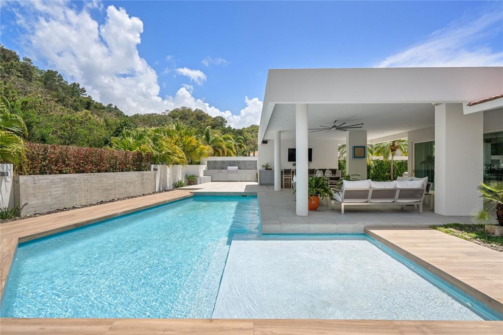 A modern living room features a textured gray wall, a wooden staircase, and a glass railing — 530 CAMINO DE GUILLARTE, DORADO, PR, PR