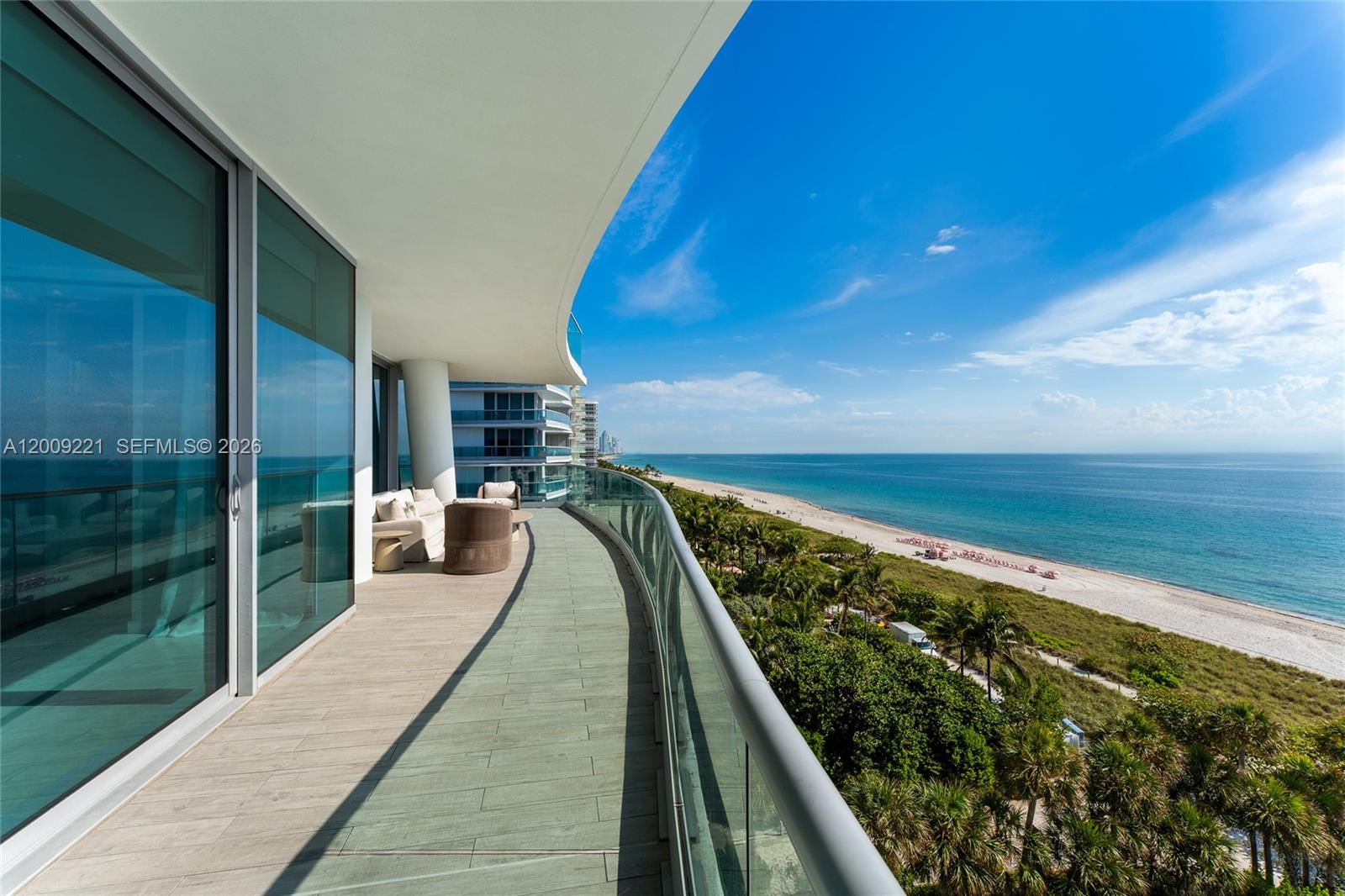 A curved balcony with wood-look tile flooring overlooks the ocean and a sandy beach — 9349 Collins Ave # 801, Surfside FL 33154, SURFSIDE, FL