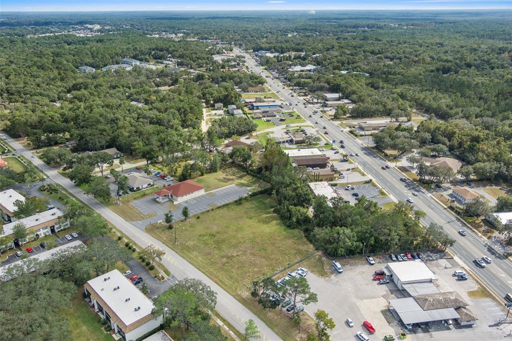An aerial view shows a vacant lot surrounded by commercial buildings, parking lots, and trees — 2514 HIGHWAY 44 W, INVERNESS, FL