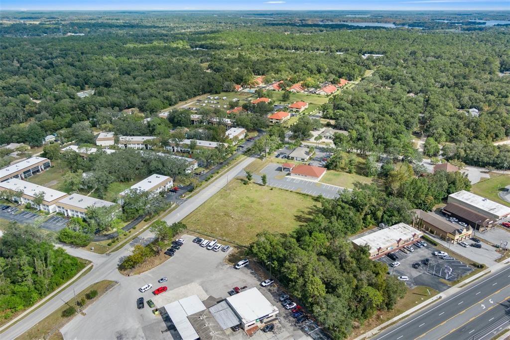An aerial view shows a commercial building, a vacant lot, and apartment complexes surrounded by trees — 2514 HIGHWAY 44 W, INVERNESS, FL