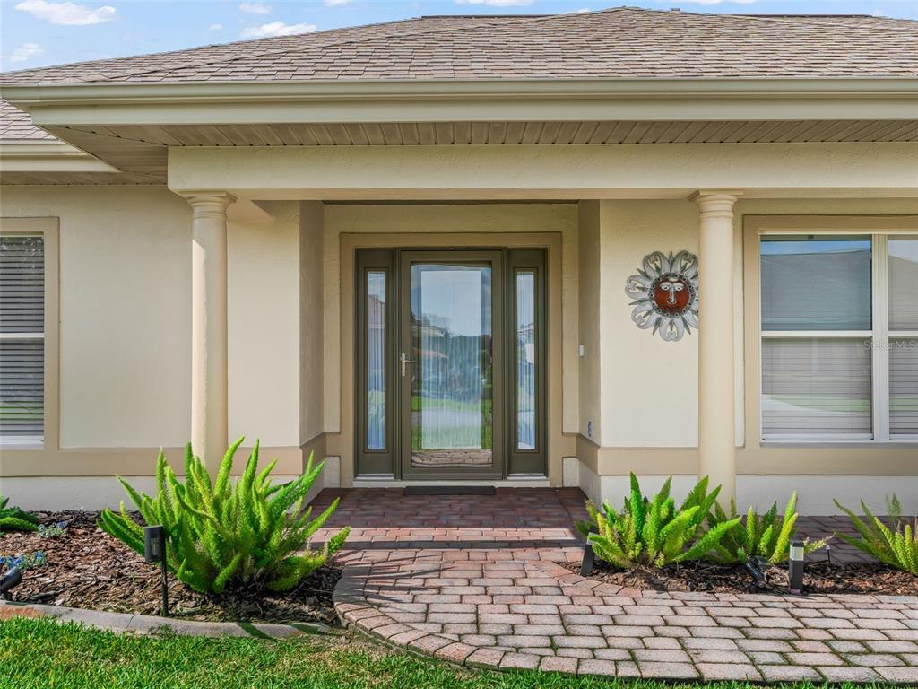 A front entrance with a glass door, two columns, and a brick walkway with landscaping — 11086 SE 175TH PLACE, SUMMERFIELD, FL