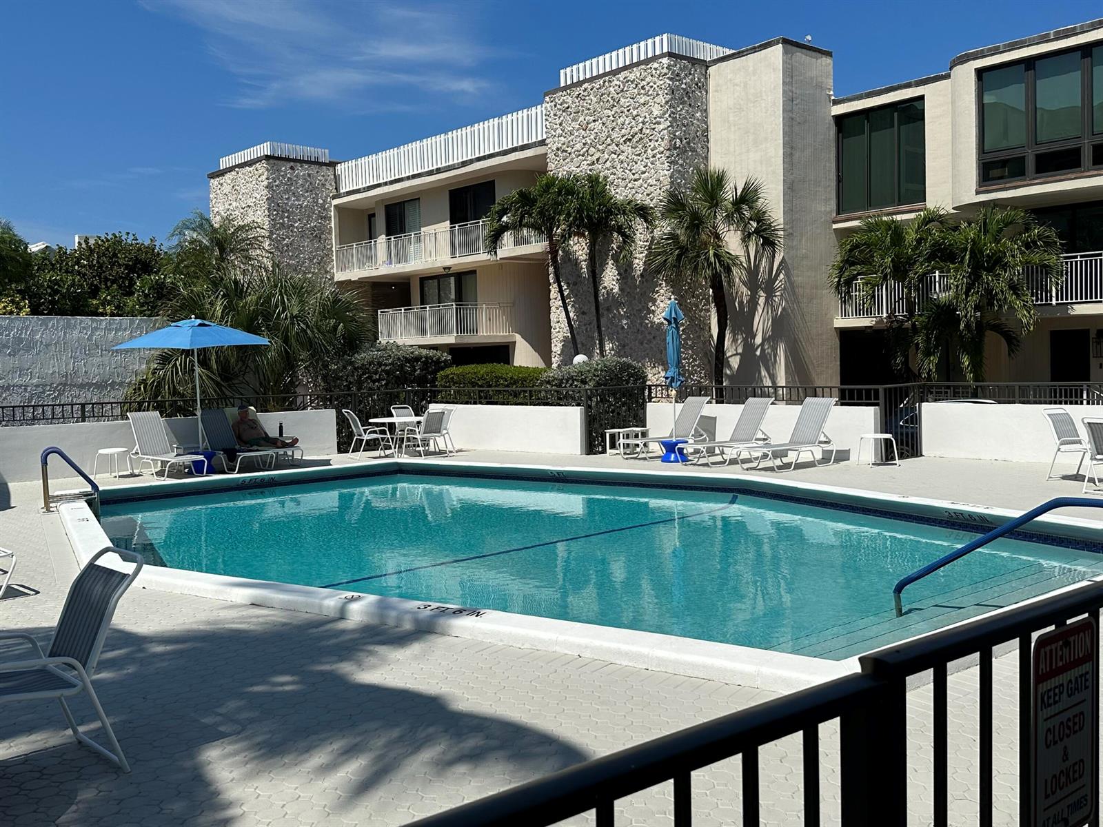A swimming pool with lounge chairs and umbrellas sits in front of a multi-story building — 2175 S Ocean Boulevard # 103, Delray Beach FL 33483, DELRAY BEACH, FL