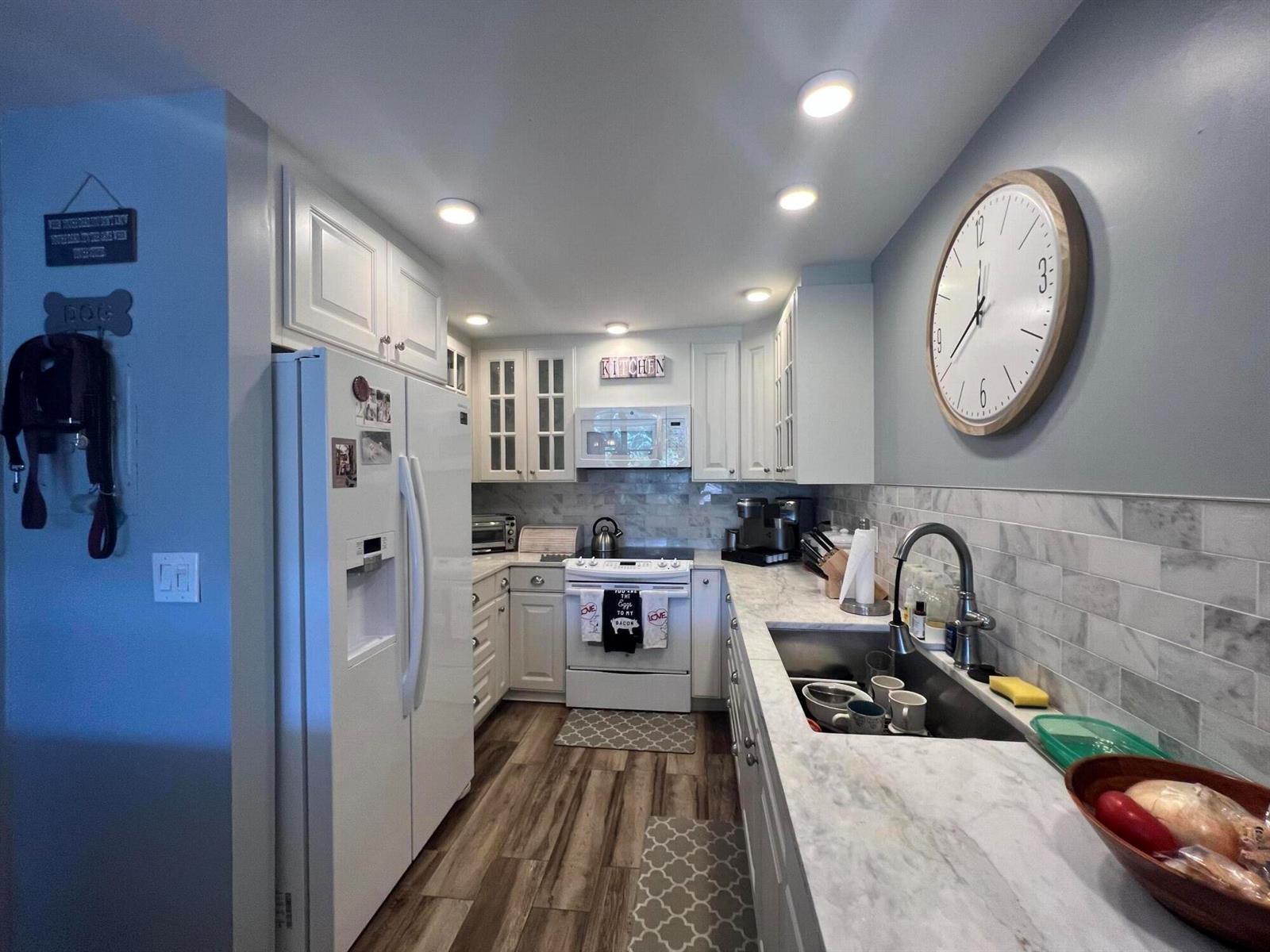 A kitchen with white cabinets, marble-look countertops, stainless steel appliances, and a large wall clock — 2175 S Ocean Boulevard # 103, Delray Beach FL 33483, DELRAY BEACH, FL
