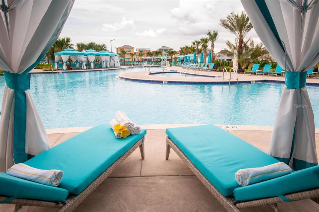 Two turquoise lounge chairs sit under a cabana overlooking a large resort-style swimming pool — 2924 CARIBBEAN SOUL DRIVE, KISSIMMEE, FL