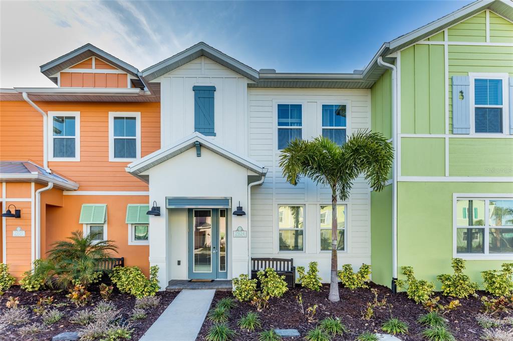 A colorful multi-unit townhouse exterior with a central entrance, palm tree, and landscaped front yard — 2924 CARIBBEAN SOUL DRIVE, KISSIMMEE, FL