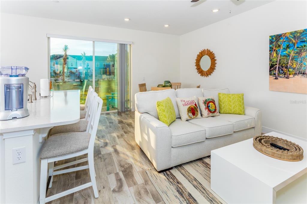 A living room and kitchen area with light wood floors, a white sofa, and sliding doors — 2924 CARIBBEAN SOUL DRIVE, KISSIMMEE, FL