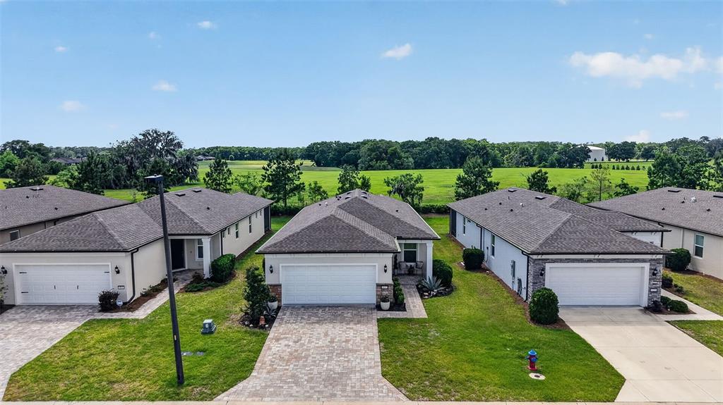 An aerial view shows three suburban houses with paved driveways and lawns facing a field — 6042 SW 93RD CIRCLE, OCALA, FL
