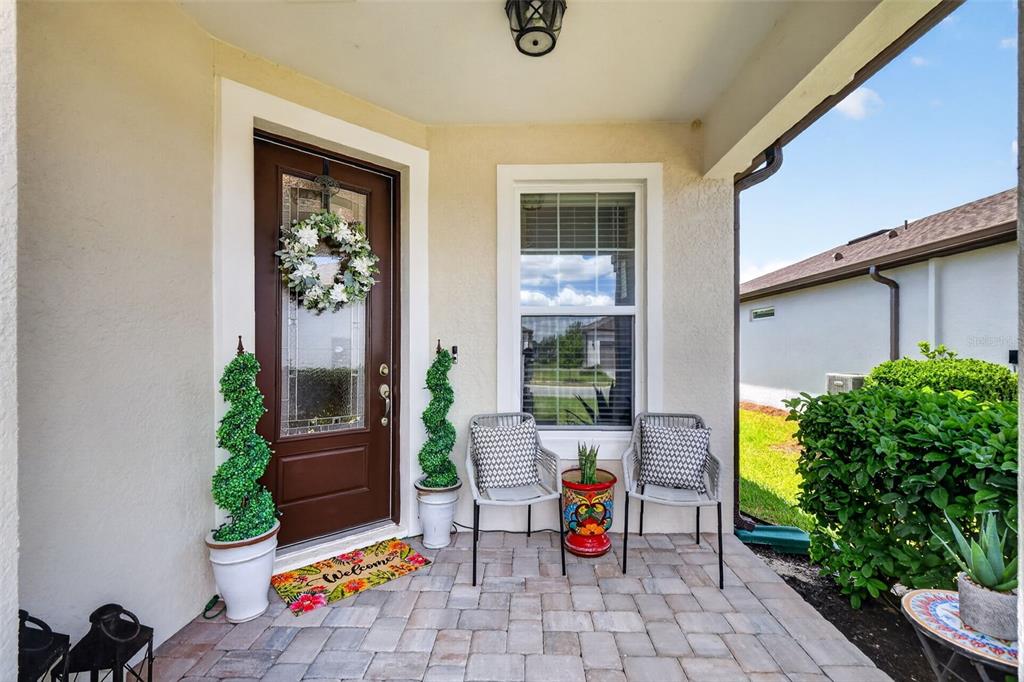 A covered front porch features a brown door, two chairs, and potted topiary plants — 6042 SW 93RD CIRCLE, OCALA, FL