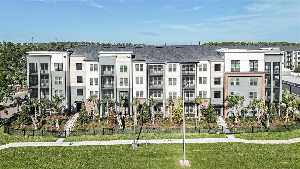An exterior view of a multi-story apartment building with a black fence and palm trees — 35820 N US HWY 19 UNIT B1, PALM HARBOR, FL