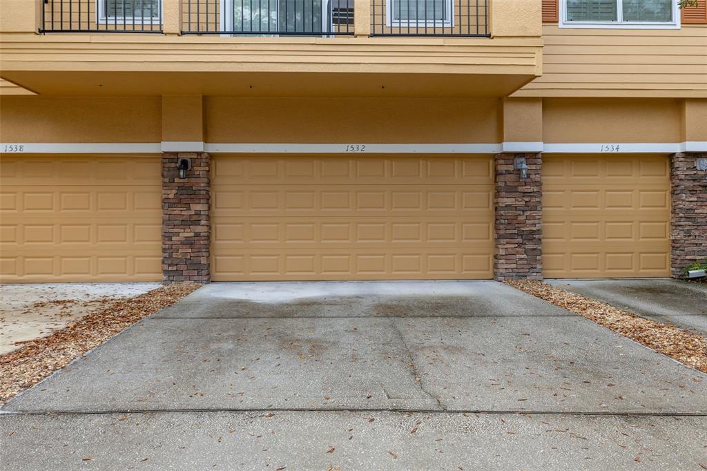 Three tan garage doors with stone pillars are set beneath a residential balcony — 1532 SCARLET OAK LOOP UNIT 70B, WINTER GARDEN, FL