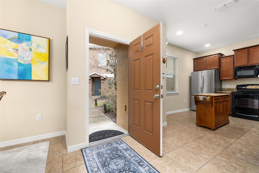 An open front door reveals an exterior walkway, leading into a kitchen with tile flooring — 1532 SCARLET OAK LOOP UNIT 70B, WINTER GARDEN, FL