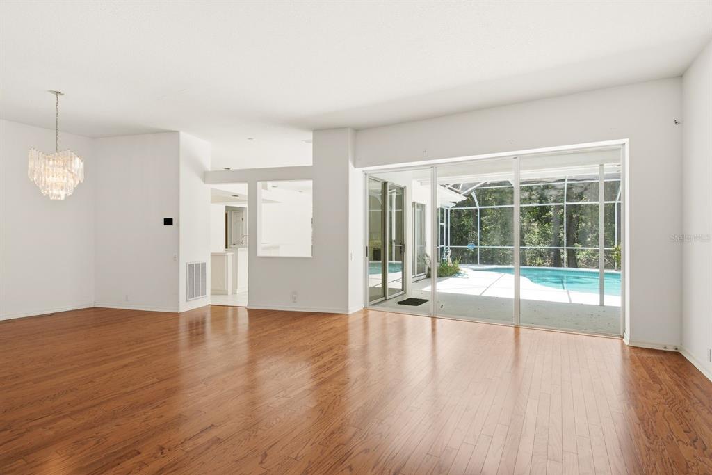 A bright living room with hardwood floors, a crystal chandelier, and sliding doors to a pool — 3951 BRIGHTSIDE LANE, PALM HARBOR, FL