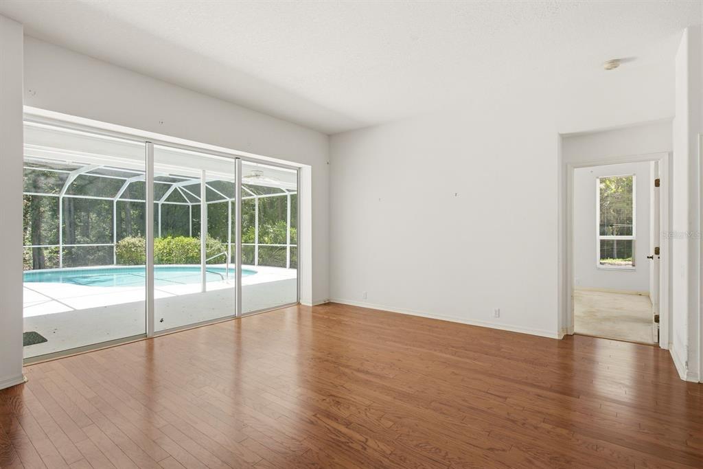 A living room with hardwood floors, large sliding glass doors, and a view of a pool — 3951 BRIGHTSIDE LANE, PALM HARBOR, FL