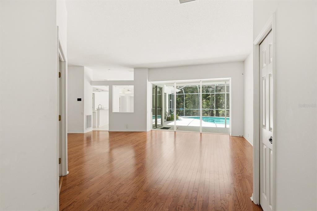 An empty room with hardwood floors, white walls, and sliding glass doors overlooking a pool — 3951 BRIGHTSIDE LANE, PALM HARBOR, FL