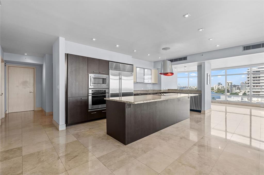 A modern kitchen features dark wood cabinetry, a large granite island, and floor-to-ceiling windows — 1052 ASHFORD AVENUE UNIT 9C, SAN JUAN, PR