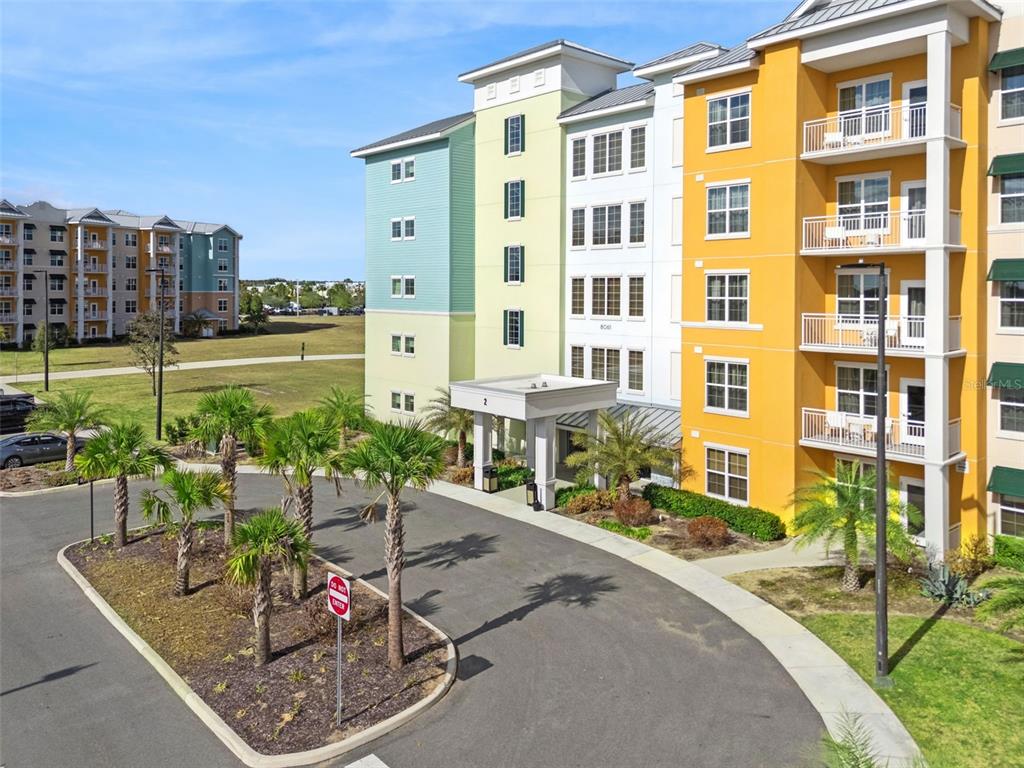 An exterior view of a multi-story apartment building with colorful facades and a circular driveway — 8061 VACATION AVENUE UNIT 2508, KISSIMMEE, FL