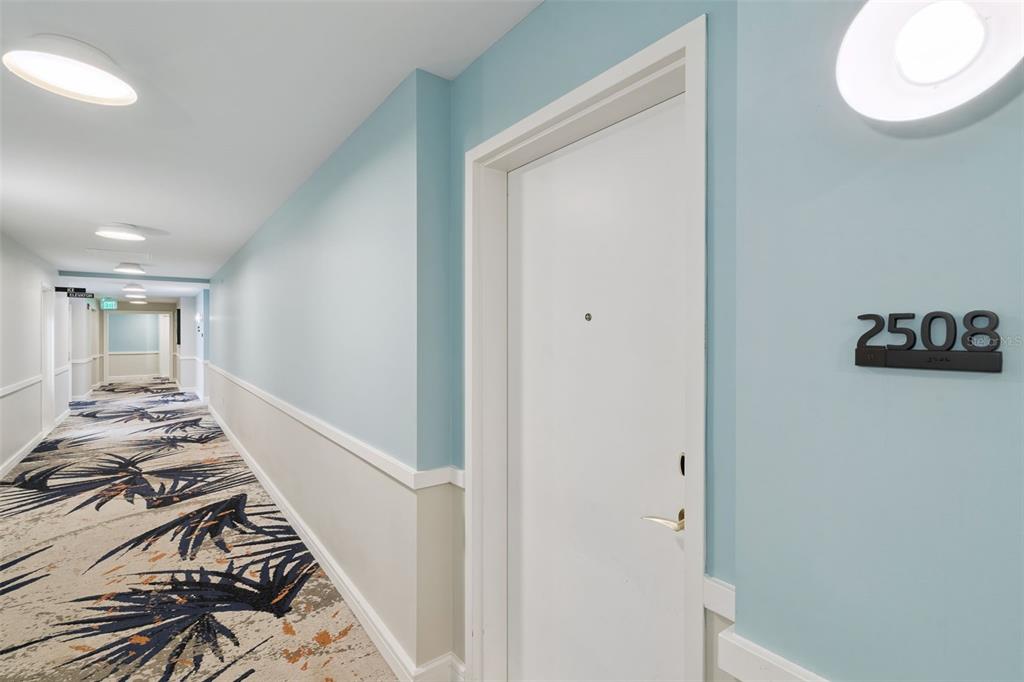 A hallway with light blue walls, patterned carpet, and a white door labeled 2508 — 8061 VACATION AVENUE UNIT 2508, KISSIMMEE, FL