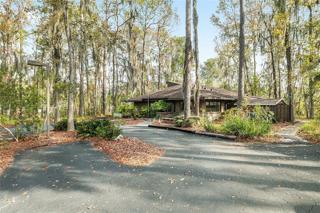 A low-slung house with a brown roof sits behind a paved driveway among tall trees — 2750 SE 17TH STREET, OCALA, FL