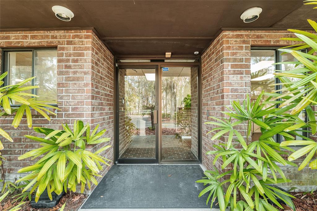 A glass-paneled entrance door is framed by brick walls and flanked by two potted palms — 2750 SE 17TH STREET, OCALA, FL