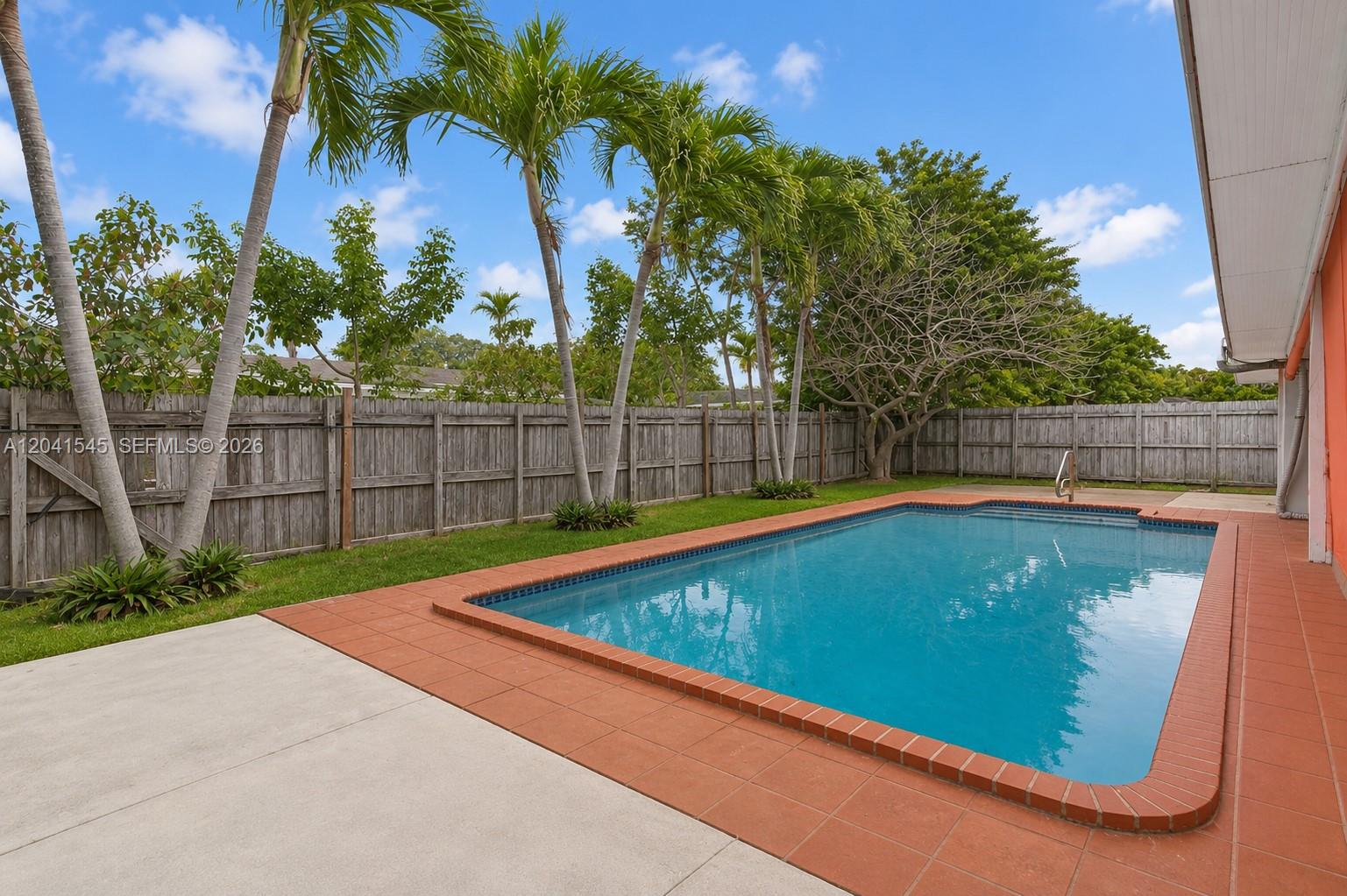 A backyard features a rectangular swimming pool surrounded by a red tile border and concrete — 18670 Belview Dr, Cutler Bay FL 33157, CUTLER BAY, FL