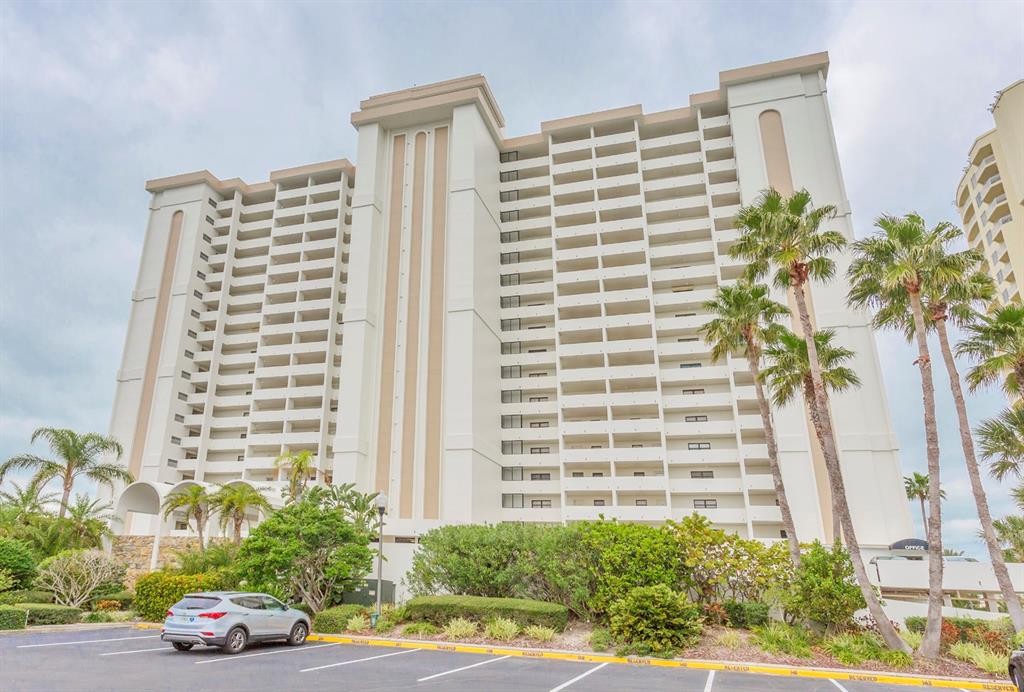 A tall, multi-story white apartment building stands behind a parking lot with palm trees — 1230 GULF BOULEVARD UNIT 508, CLEARWATER BEACH, FL