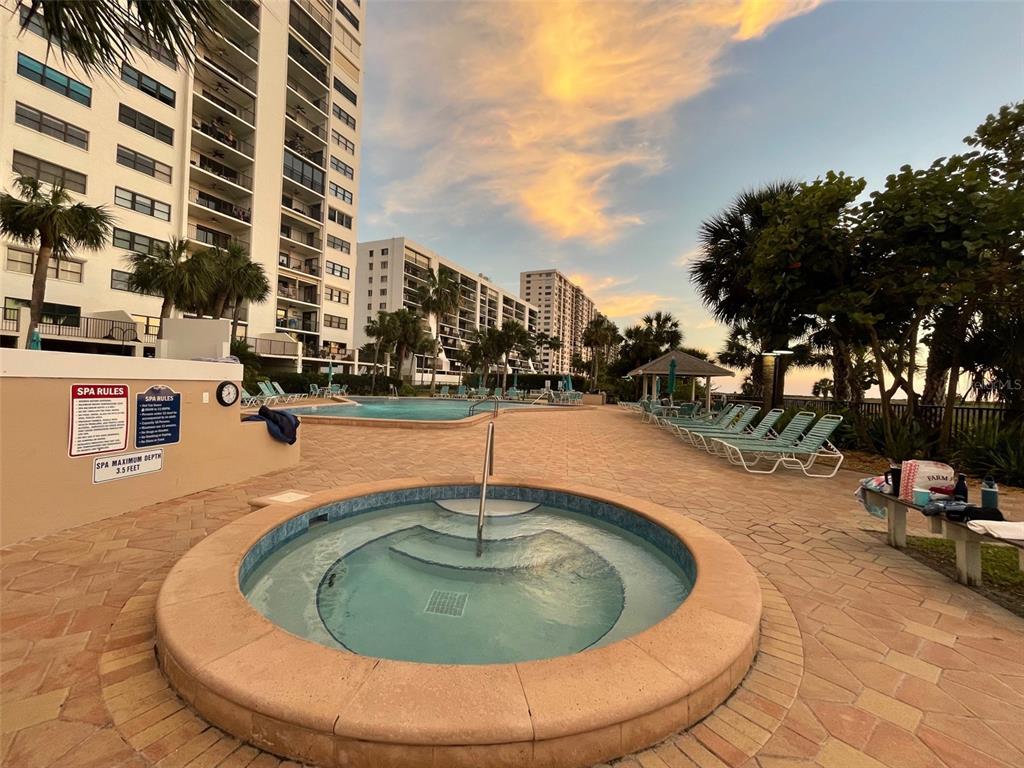 A circular spa and a swimming pool are located on a paved patio near tall buildings — 1230 GULF BOULEVARD UNIT 508, CLEARWATER BEACH, FL