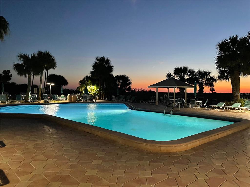 A swimming pool with lounge chairs and a gazebo at sunset — 1230 GULF BOULEVARD UNIT 508, CLEARWATER BEACH, FL