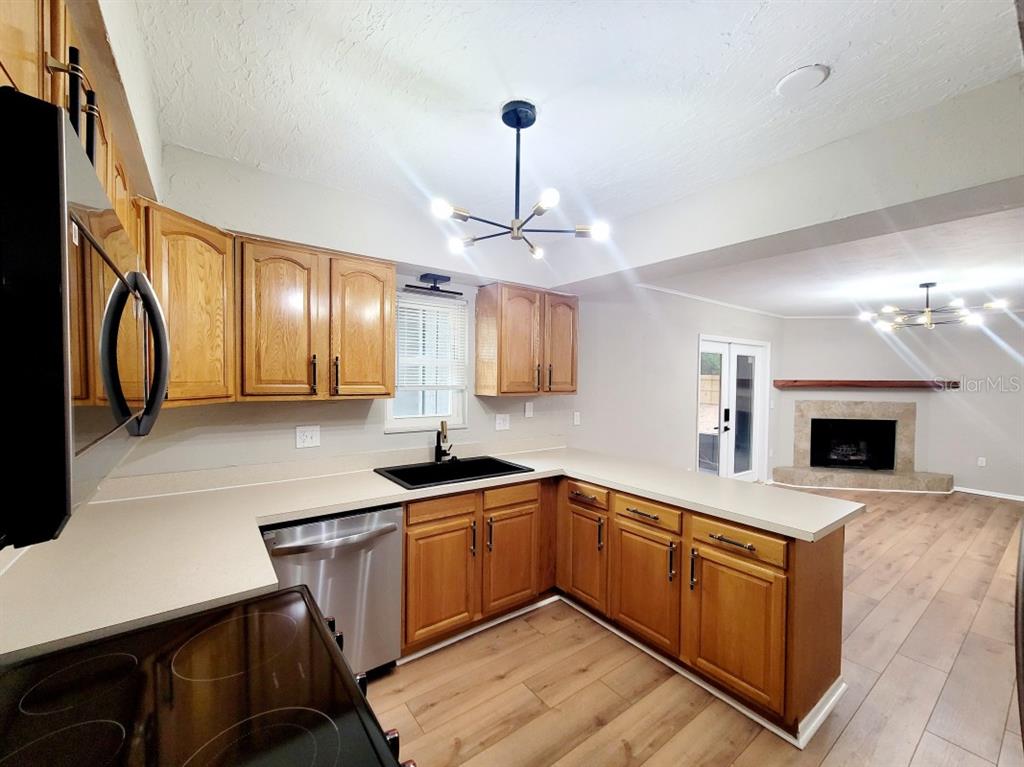 A kitchen with wood cabinets, stainless steel appliances, and a black sink overlooks a living area — 3116 W UNIVERSITY AVENUE, GAINESVILLE, FL