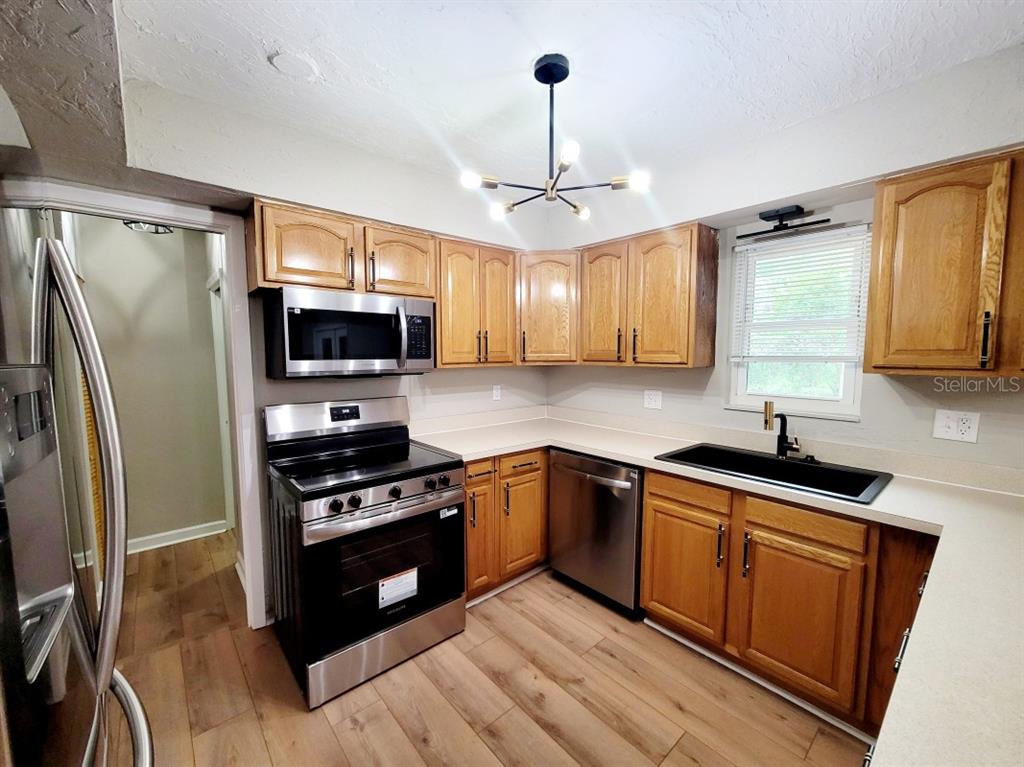 A kitchen features wood cabinets, stainless steel appliances, a black sink, and light wood flooring — 3116 W UNIVERSITY AVENUE, GAINESVILLE, FL