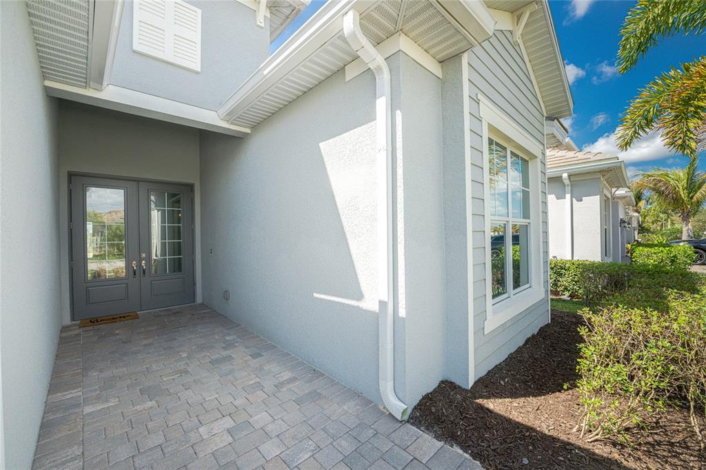 A paved entryway leads to a gray double front door on a light blue house — 25223 KEYGRASS COURT, PUNTA GORDA, FL